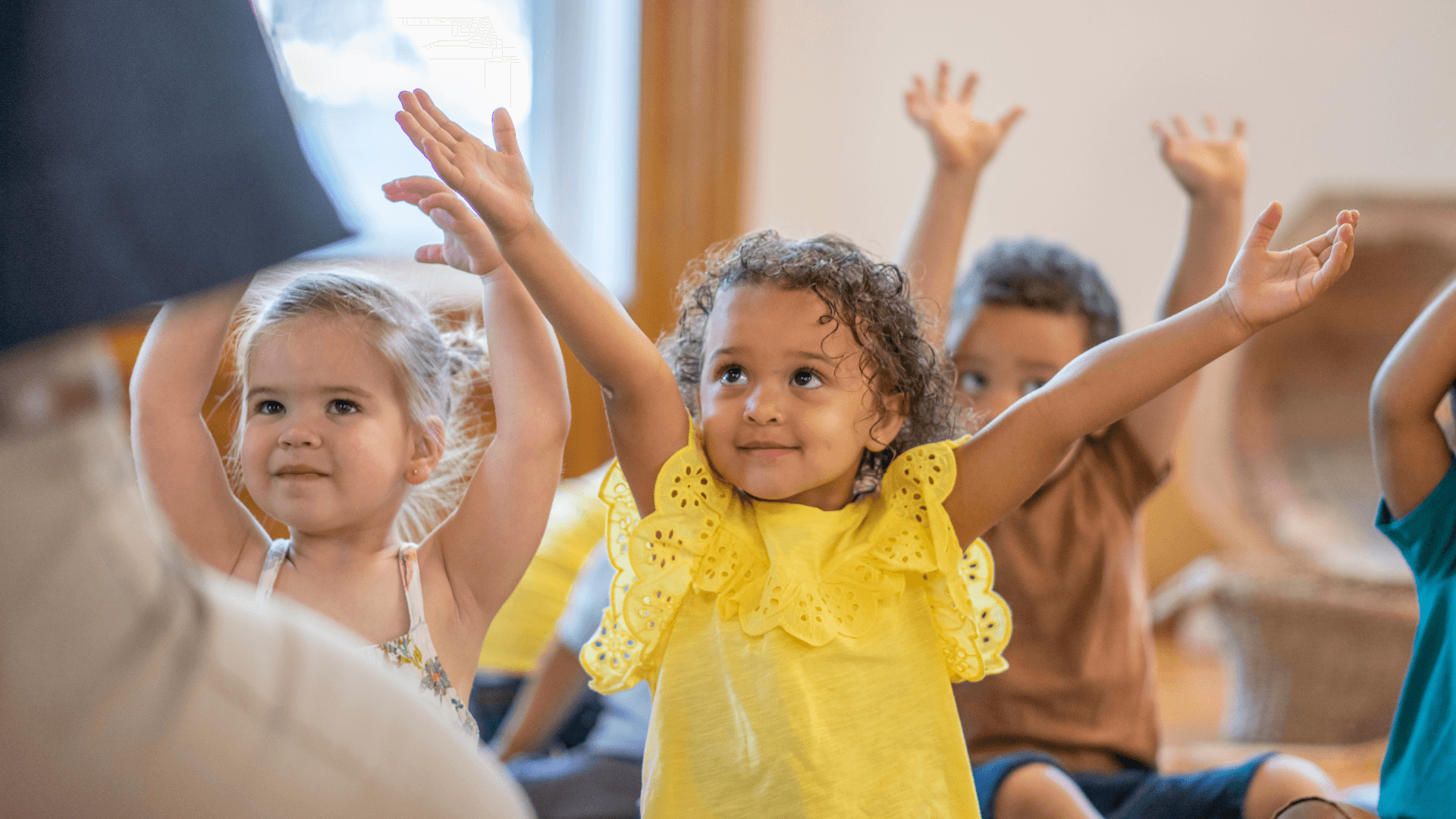 A group of young kids joyfully raising their hands during a learning activity